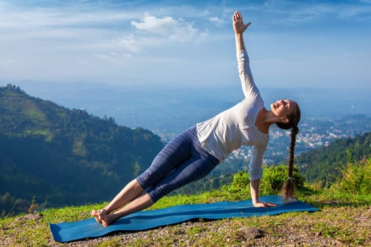 Yoga outdoors - beautiful sporty fit woman doing yoga asana Vasisthasana - side plank pose in mountains