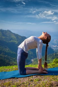 Yoga - outdoors young beautiful slender woman yoga instructor doing camel pose Ustrasana asana exercise outdoors in mountains in the morning