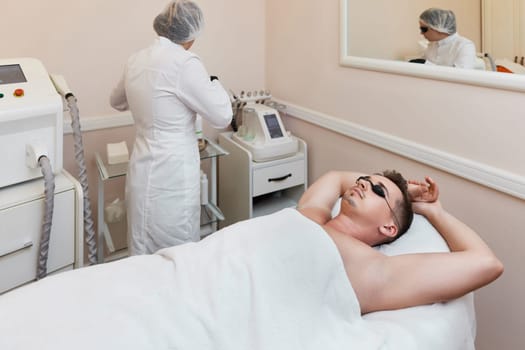 young man with protective goggles undergoes procedure of arm pit laser epilation in clinic