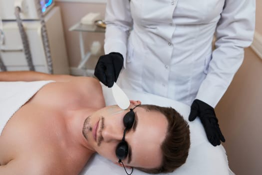 beautician applies cooling gel to male facefor receiving epilation in beauty center.