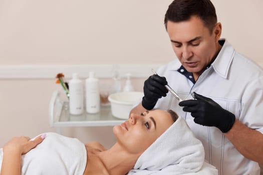 male beautician applies the mask to the face of beautiful woman in the spa salon. facial skin care concept.