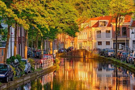 Delt canal with old houses and cars parked along on sunset. Delft, Netherlands