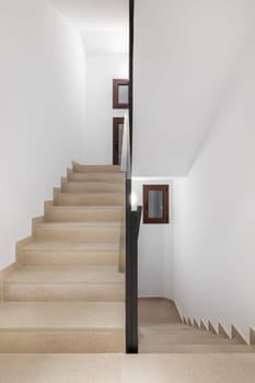 Vertical photo of a clean comfortable staircase with beige walkway black metal railings and white walls in a hotel in a cozy new urban area. Copyspace.