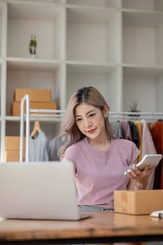 Female online seller preparing delivery items and using calculator to calculate orders.