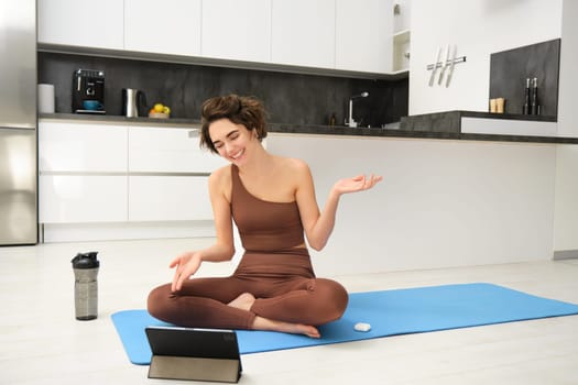 Woman, fitness instructor sitting on rubber mat, yoga couch talking to online group, recording class on tablet, remote training outside of gym, workout from home.