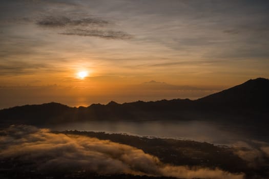 Amazing sunrise lake view at mount Batur. Dawns landscape photo at foggy Batur mount with orange sky