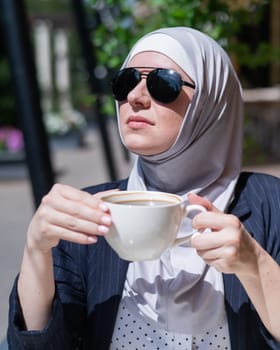 Caucasian woman in hijab drinking coffee in outdoor cafe