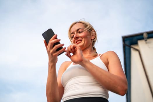 Beautiful blonde caucasian woman using phone while doing sports outdoors. Healthy fitness lifestyle, summer workout in city. Using technology for tracking activity. High quality photo