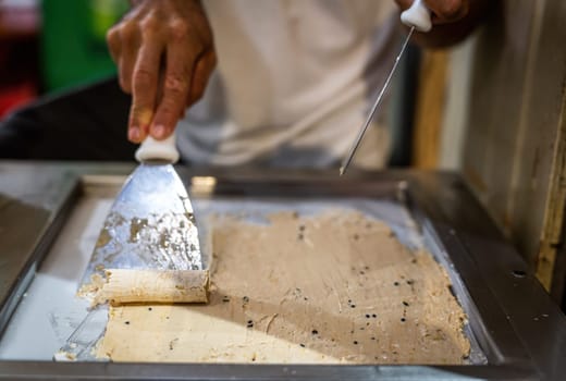 A man expertly creates fresh passion fruit ice cream on a metal plate, crafting beautiful spirals.