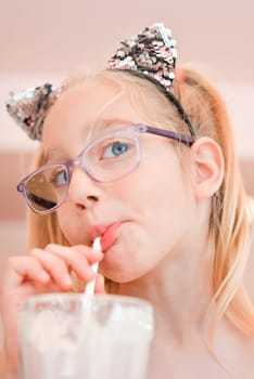 Little pretty girl seven years old drinking strawberry milkshake through a straw in a coffee shop. Portrait of The happy girl drinking a cocktail through a straw.