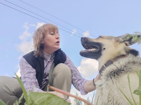 A girl or a woman and a German shepherd or Eastern European Shepherd dog in the forest, in nature, on spring, summer, or autumn day and blue sky. The concept of friendship between humans and animals