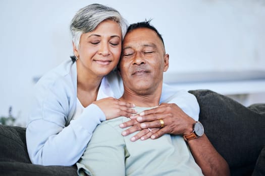 Love, romance and a senior couple on a sofa in the living room of their home together during retirement. Happy, relax and hug with an elderly woman embracing her husband for comfort in a house.