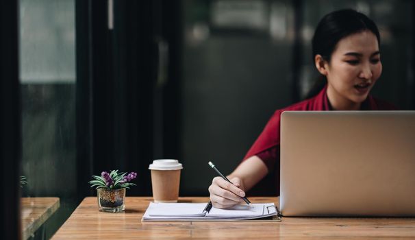 Cropped photo of woman writing making list taking notes in notepad working or learning on laptop indoors- educational course or training, seminar, education online concept.