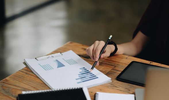 Close up business woman holding pen and pointing paper chart summary analyzing annual business report with using laptop at room office desk.