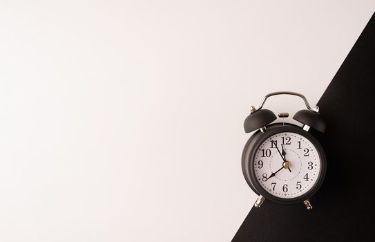 Time management, punctuality, business metaphors. White vintage alarm clock with nine ten on double white and black background, flat lay top view, copy space.