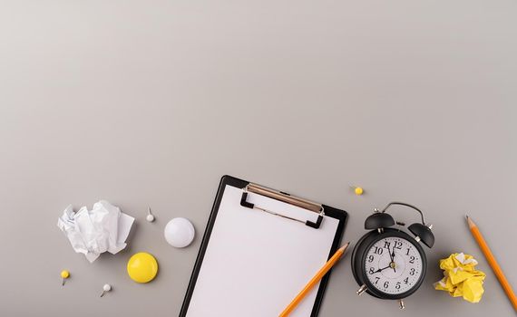 Business planning, time management concept. Blank paper on clipboard, white alarm clock and stationery top view on gray table. Copy space, flat lay