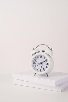 Time management, punctuality, business metaphors. Back to school. White alarm clock hands on nine ten on stack of books, mockup design, copy space