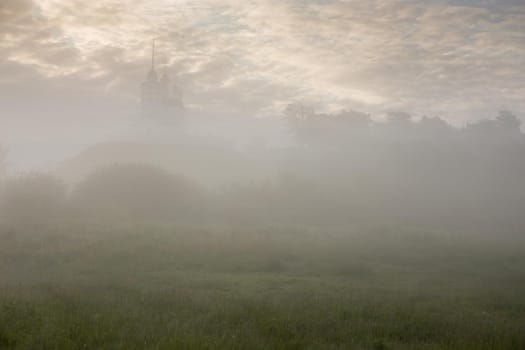 foggy summer morning landscape with the church on the hill in the background.