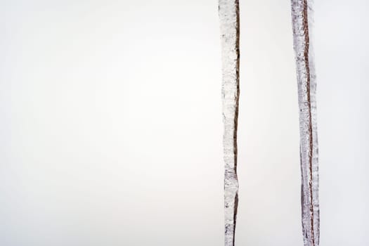 Two icicles hanging from roof, white overcast background, space for text on left side.