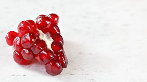 Cluster of pomegranate (Punica granatum) gem like fruits on white working board, banner with space for text on right side.