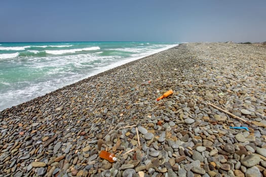 Various plastic rubbish on wild unspoiled black pebble stone beach, beautiful sea in background.