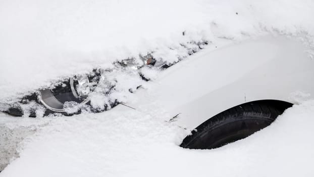 Car hidden in deep snowload, detail on front light and part of tire showing under snow.