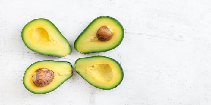 Overhead shot - four avocado halves, two with seed visible, on white working board; wide banner space for text at right side.