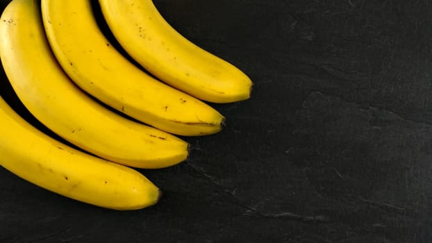 Top down view, four bananas on black slate board, space for text on right side.