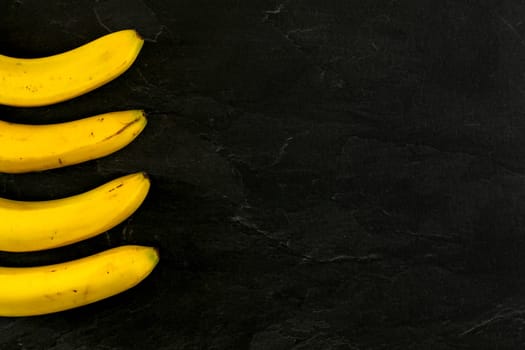 Four bananas on black slate like board photo from above, only part of them visible, more space for text right side.