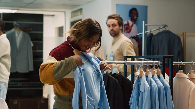 African american client doing shopping for formal wear, examining new retail store merchandise. Young woman checking fashion boutique clothes in clothing store, commercial activity. Tripod shot.