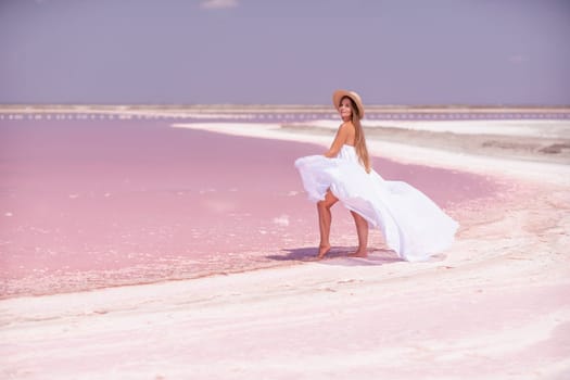 Woman in pink salt lake. She in a white dress and hat enjoys the scenic view of a pink salt lake as she walks along the white, salty shore, creating a lasting memory