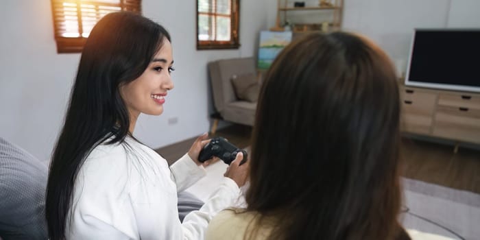 Asian homosexual couple sitting on couch turn to meet each other eyes in living room at home enjoy console playing game together.