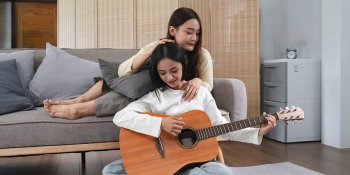 Homosexual LGBT young women playing guitar and singing in living room with happiness moment.