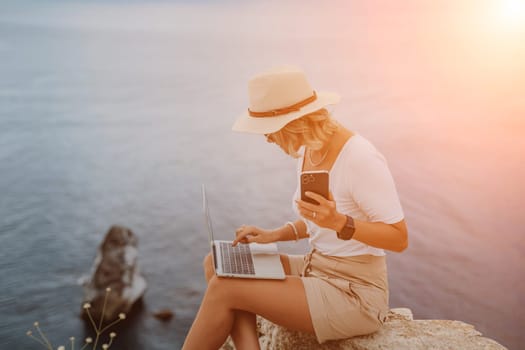 Freelance women sea working on the computer. Good looking middle aged woman typing on a laptop keyboard outdoors with a beautiful sea view. The concept of remote work