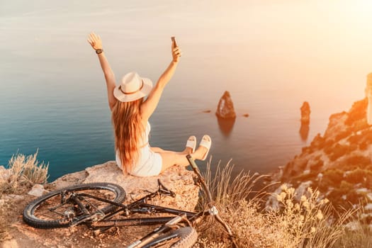 A woman cyclist on a mountain bike looking at the landscape of mountains and sea. Adventure travel on bike