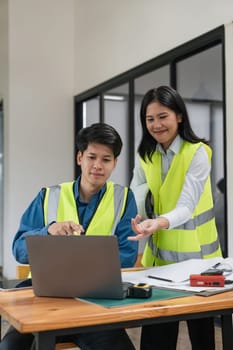 Two young man and woman engineers meeting, working, discussing, planing, designing, measuring layout of building blueprints in construction site floor at factory.