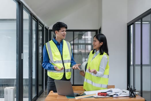 Two young man and woman engineers meeting, working, discussing, planing, designing, measuring layout of building blueprints in construction site floor at factory.