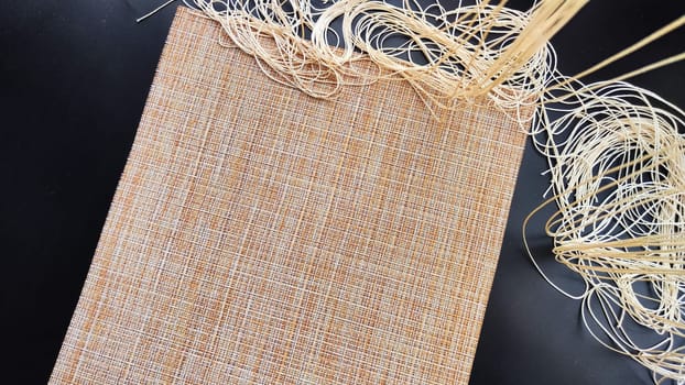 Brown or beige textured napkin, similar in weave to burlap on a black surface. Background, texture, frame and copy space. The concept of beautiful decor and comfort in house