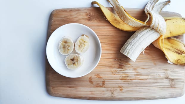 Banana with open panel on wooden board and sliced round pieces on the plate on white background. Ripe banana with peel and cooking. Delicious sweet fruit dessert. Close up