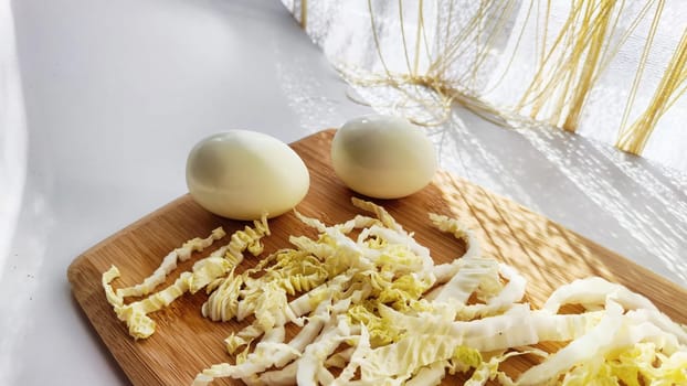 Chopped Peking cabbage and peeled eggs on cutting board as background. Cooking a healthy eco-friendly salad from natural products. Copy space and place for text