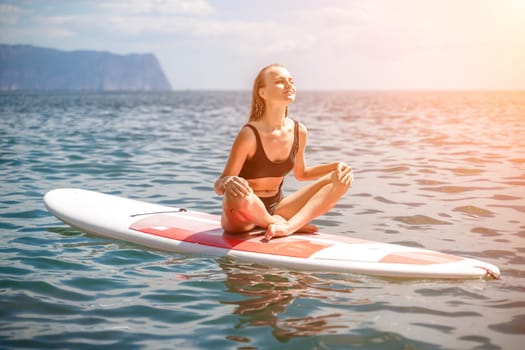 Woman sup sea. Sports girl on a surfboard in the sea on a sunny summer day. In a black bathing suit, he sits on a sapa in the sea. Rest on the sea