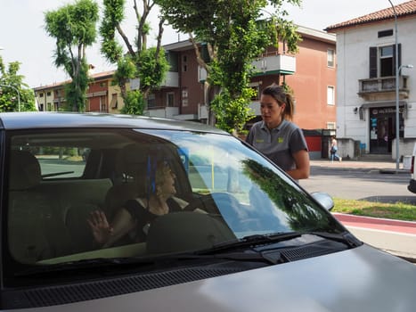 Cremona, Italy - July 3 2023 gas station attendant woman taking payments with credit card from customers outdoors near fuel pumps