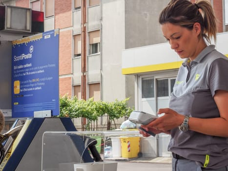 Cremona, Italy - July 3 2023 gas station attendant woman taking payments with credit card from customers outdoors near fuel pumps