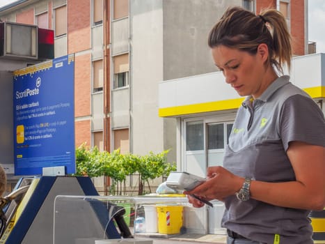 Cremona, Italy - July 3 2023 gas station attendant woman taking payments with credit card from customers outdoors near fuel pumps