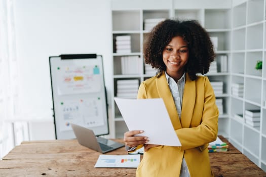 Beautiful young African american businesswoman using laptop computer and paperworks with planning working on financial document, tax, exchange, accounting and Financial advisor.