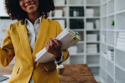 Beautiful young African american businesswoman using laptop computer and paperworks with planning working on financial document, tax, exchange, accounting and Financial advisor.