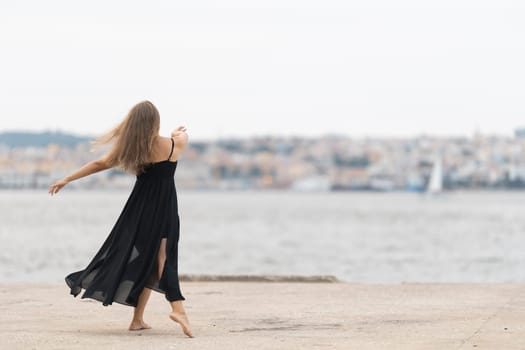 A woman in black dress dancing on the pier - view from the back. Mid shot