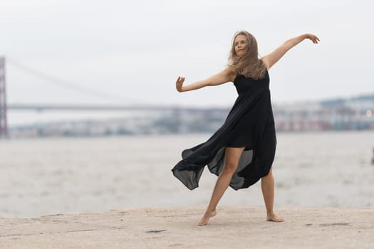 An adult woman in black dress dancing on the pier. Mid shot