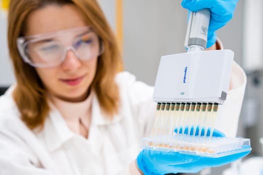 Scientist in goggles and lab coat employs a multichannel pipette Eppendorf dispenser to load microplates for immunoassay, July 2023, San Francisco, USA.