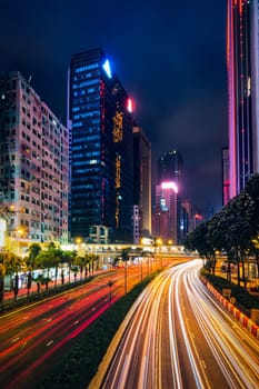 Street traffic in Hong Kong at night. Office skyscraper buildings and busy traffic on highway road with blurred cars light trails. Hong Kong, China